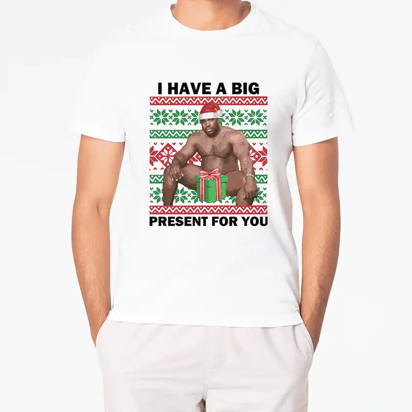 Biały t-shirt z grafiką półnagiego mężczyzny w czapce Mikołaja i napisem 'I HAVE A BIG PRESENT FOR YOU'